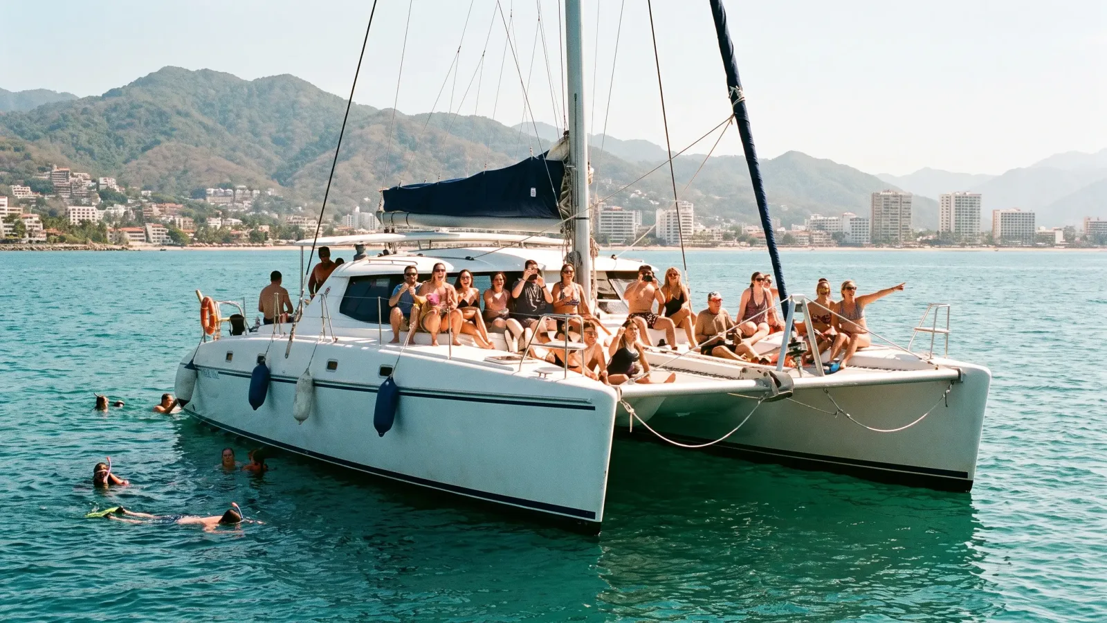 Catamaran full of tourists on a boat tour in Banderas Bay with Puerto Vallarta and the Sierra Madre behind